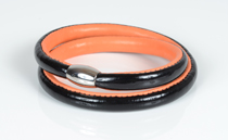 Armbånd i sort lak læder og orange lammeskind. 2 omgange med magnetlås i stål. Tykkelse 7,5 mm.